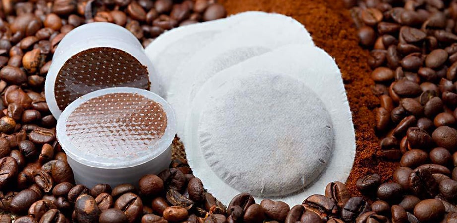 cialde e capsule di caffè poggiate su chicchi e polvere di caffè